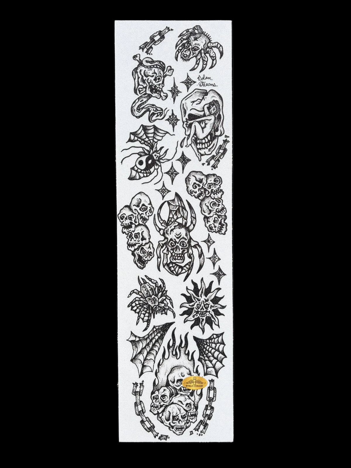 A long white sheet covered with black gothic and horror-themed temporary tattoo designs, photographed outdoors on dark asphalt with a photographer's shadow visible in the lower left corner.