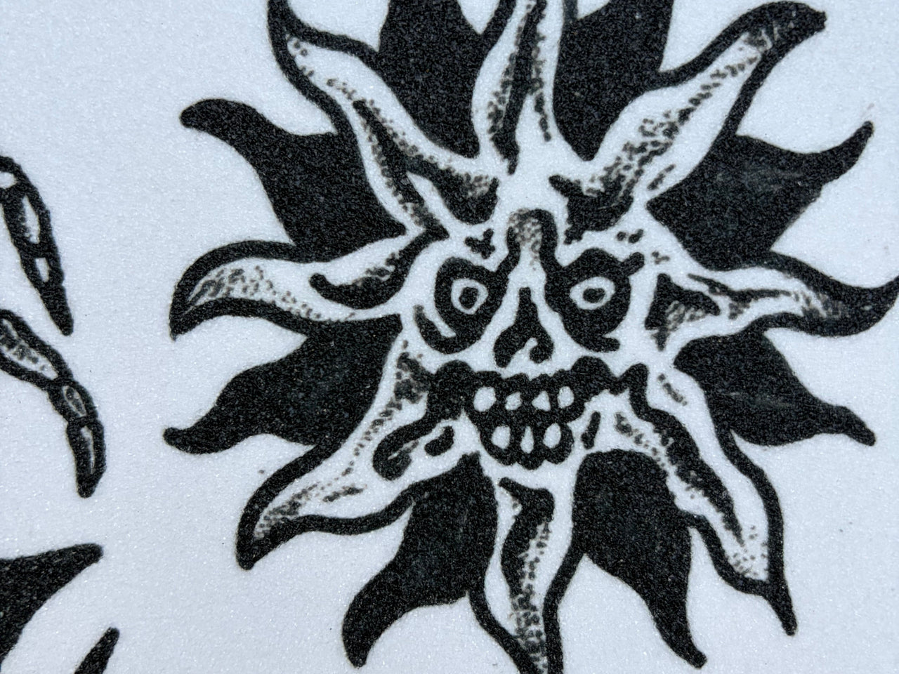 A long white sheet covered with black gothic and horror-themed temporary tattoo designs, photographed outdoors on dark asphalt with a photographer's shadow visible in the lower left corner.