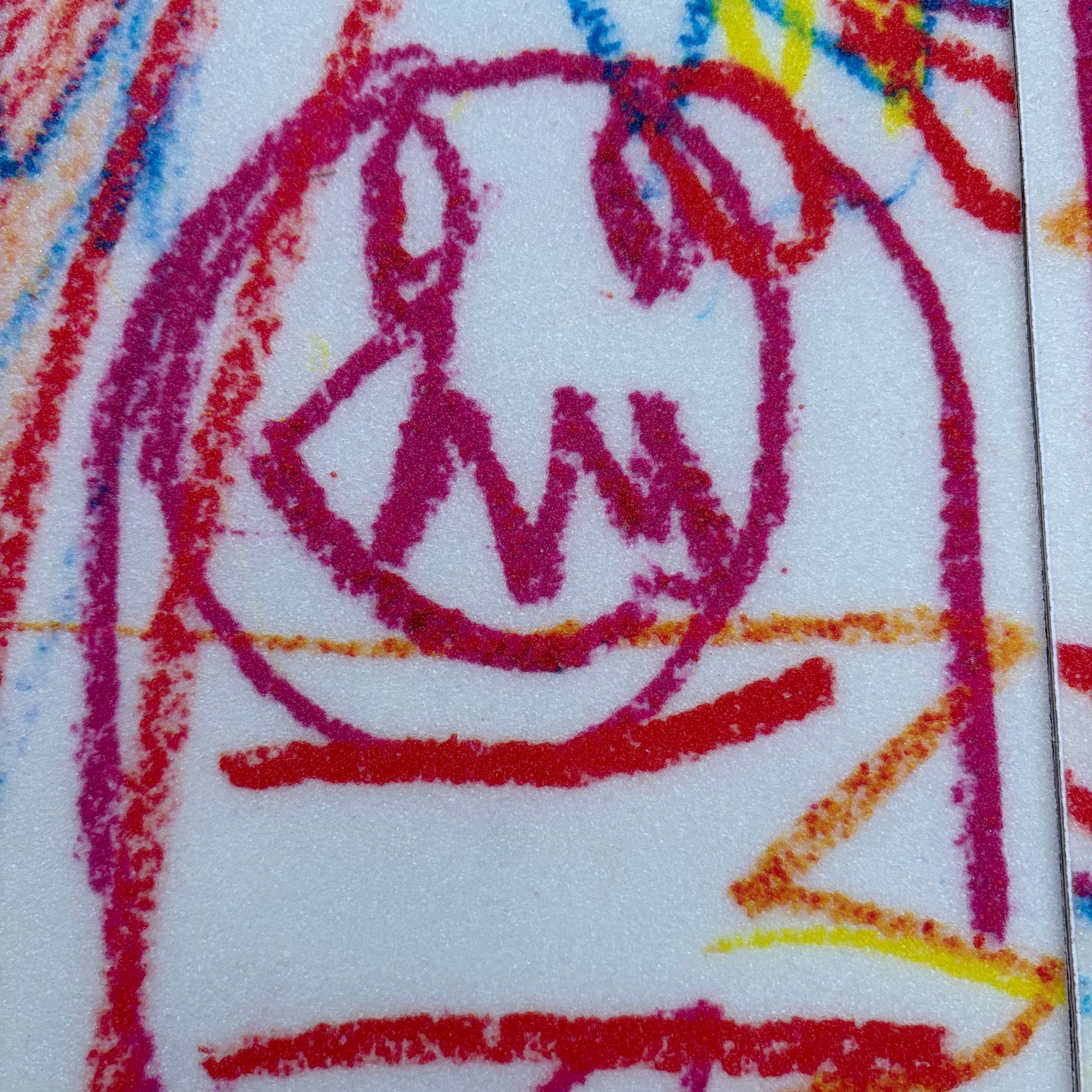 A close-up of a white surface covered with colorful crayon-like scribbles and a rough magenta circular drawing.